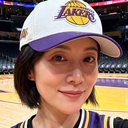 一位短发年轻女性球迷头像，约28岁，戴着湖人队棒球帽，背景为篮球场看台